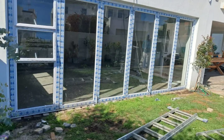 White aluminium folding doors and windows, still taped, on a garden-facing wall