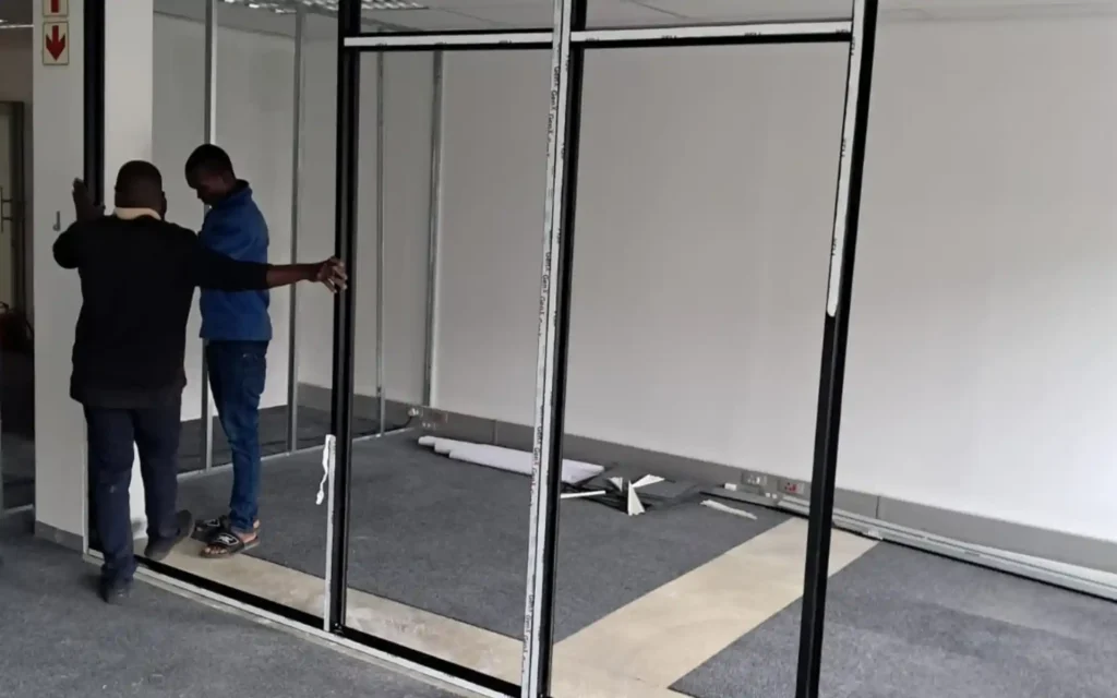 Installers fitting a black aluminium partition frame in an office